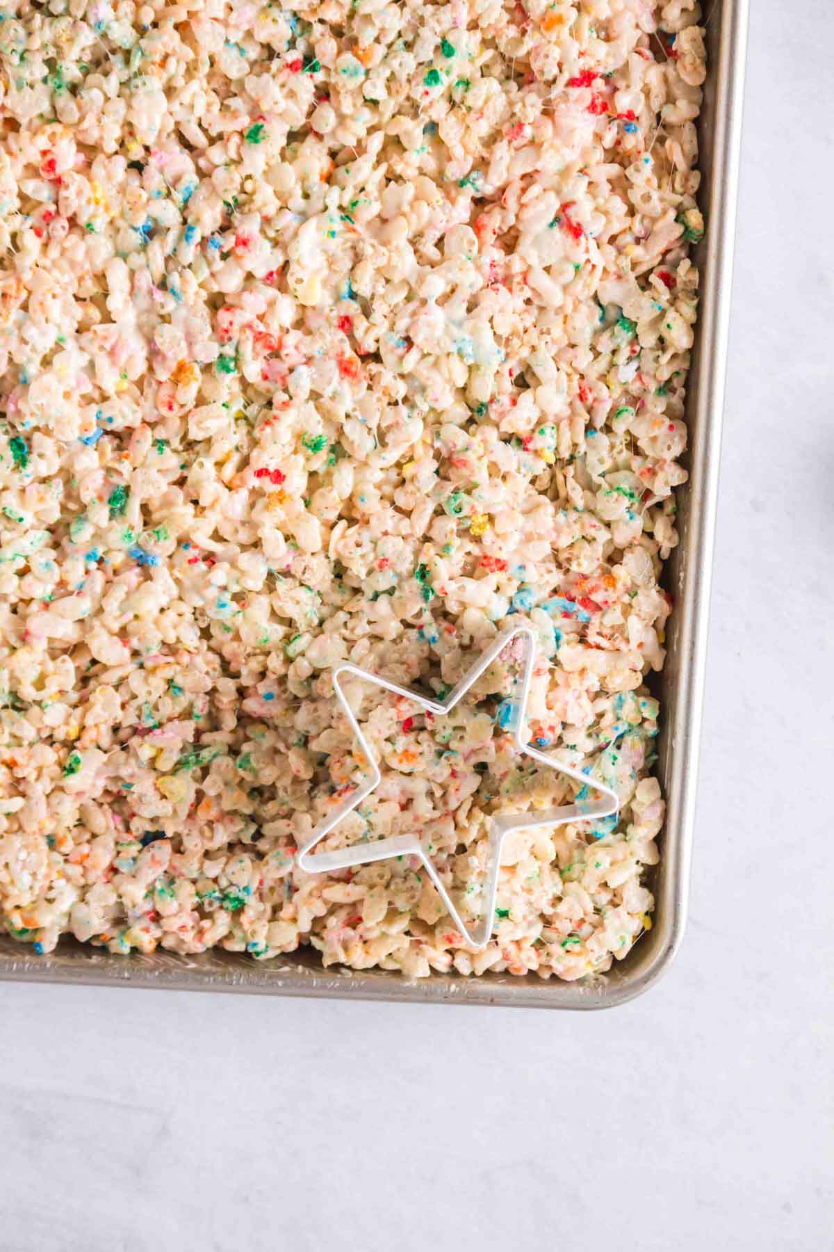 Rice Krispie Treats with Sprinkles and white chocolate being cut with a star cookie cutter.