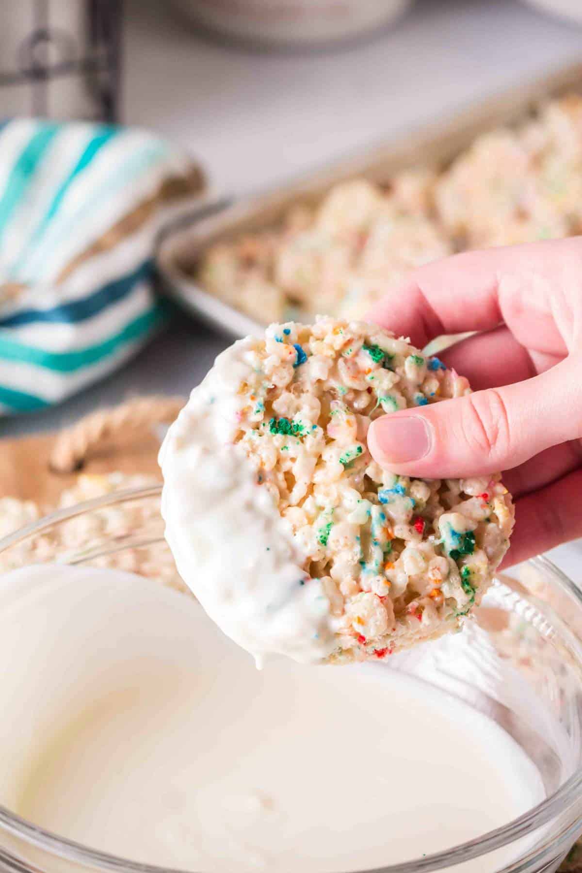 Rice Krispie Treats with Sprinkles and white chocolate being dipped in white chocolate.