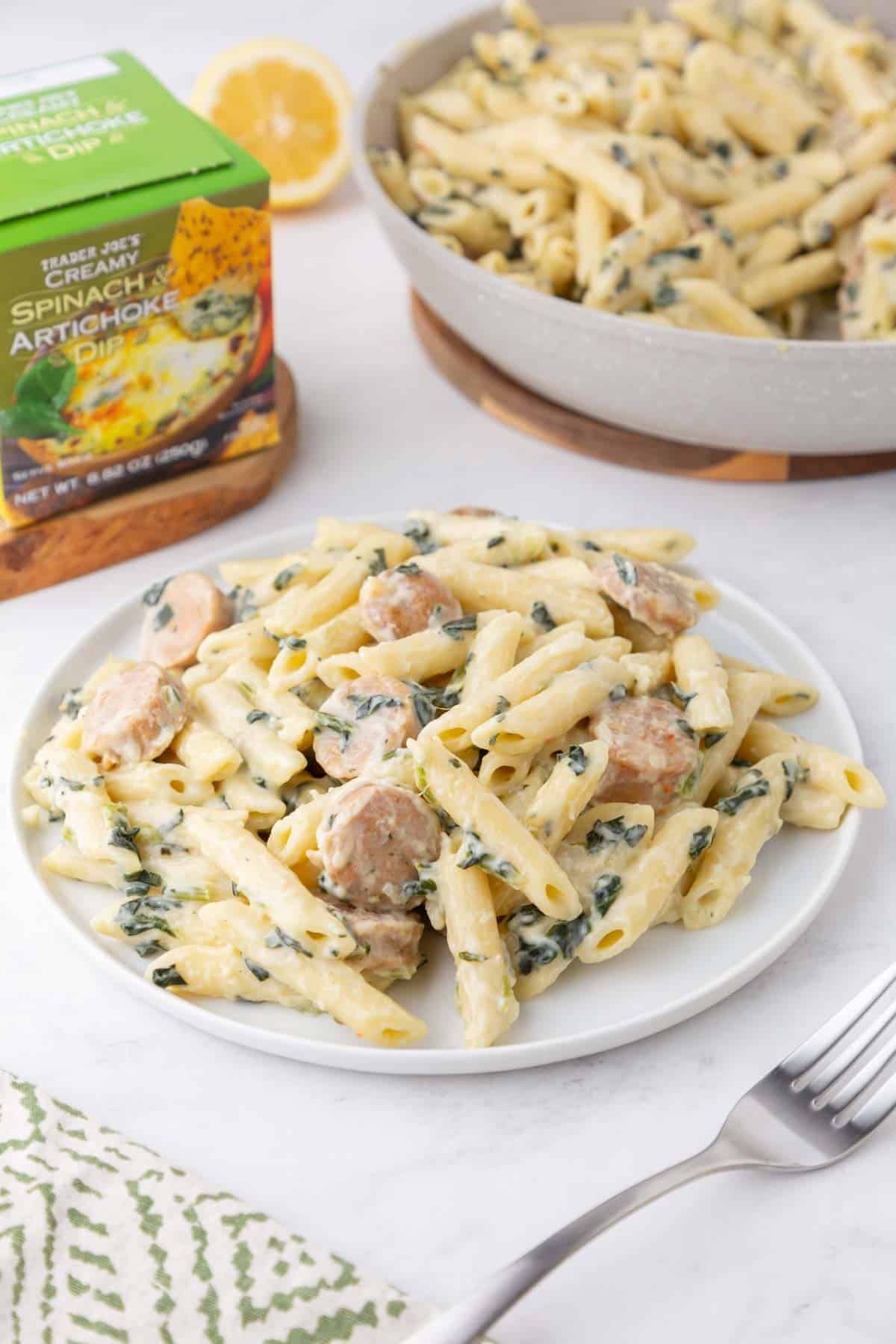 A plate of Trader Joe's Spinach and Artichoke pasta with sausage on a white plate.