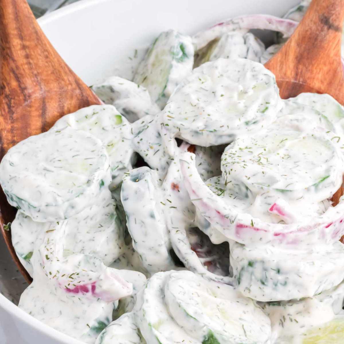 Creamy cucumber salad with mayo and dill in a large bowl with a wooden spoon.