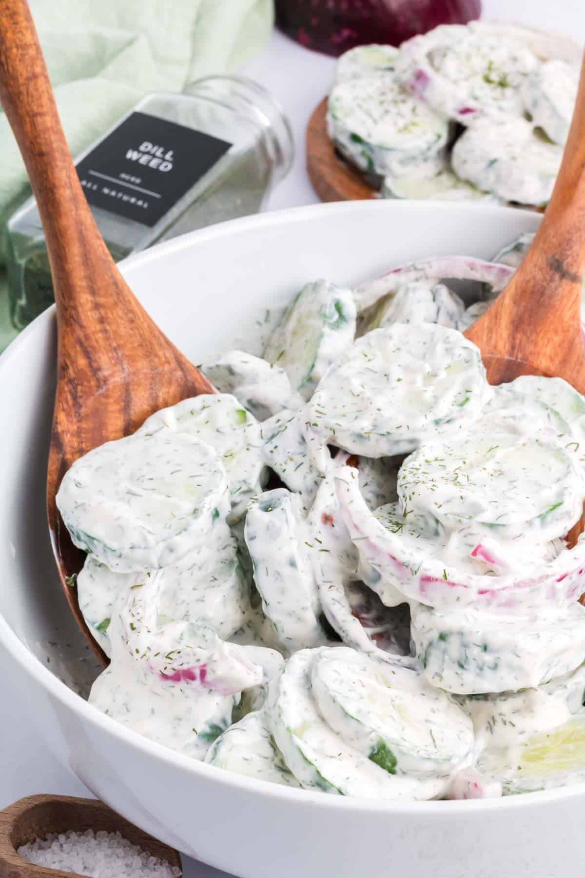 Creamy cucumber salad with mayo and sour cream in a large bowl with two wooden spoons.