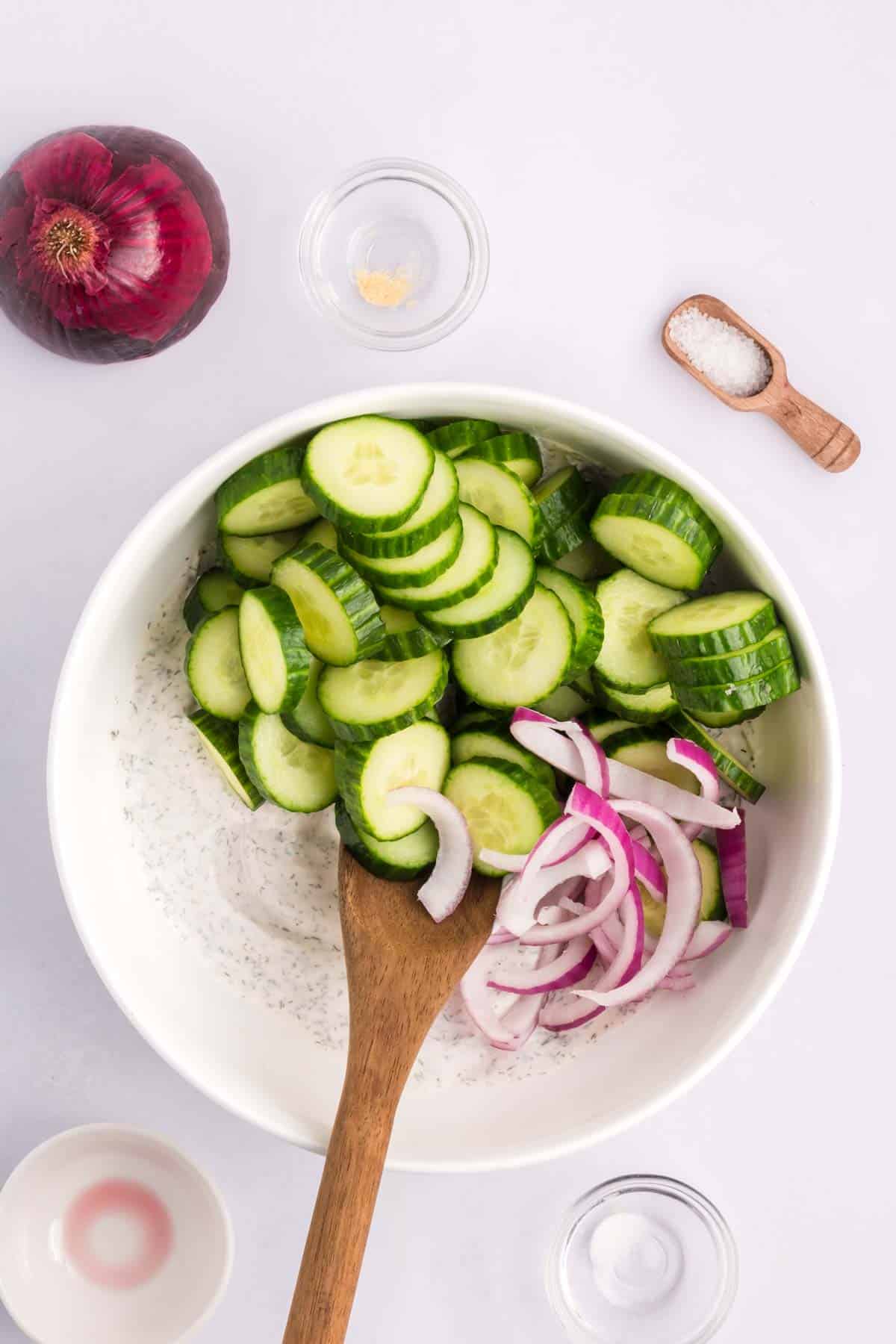 Cucumbers and red onion being mixed with the dressing in a bowl.