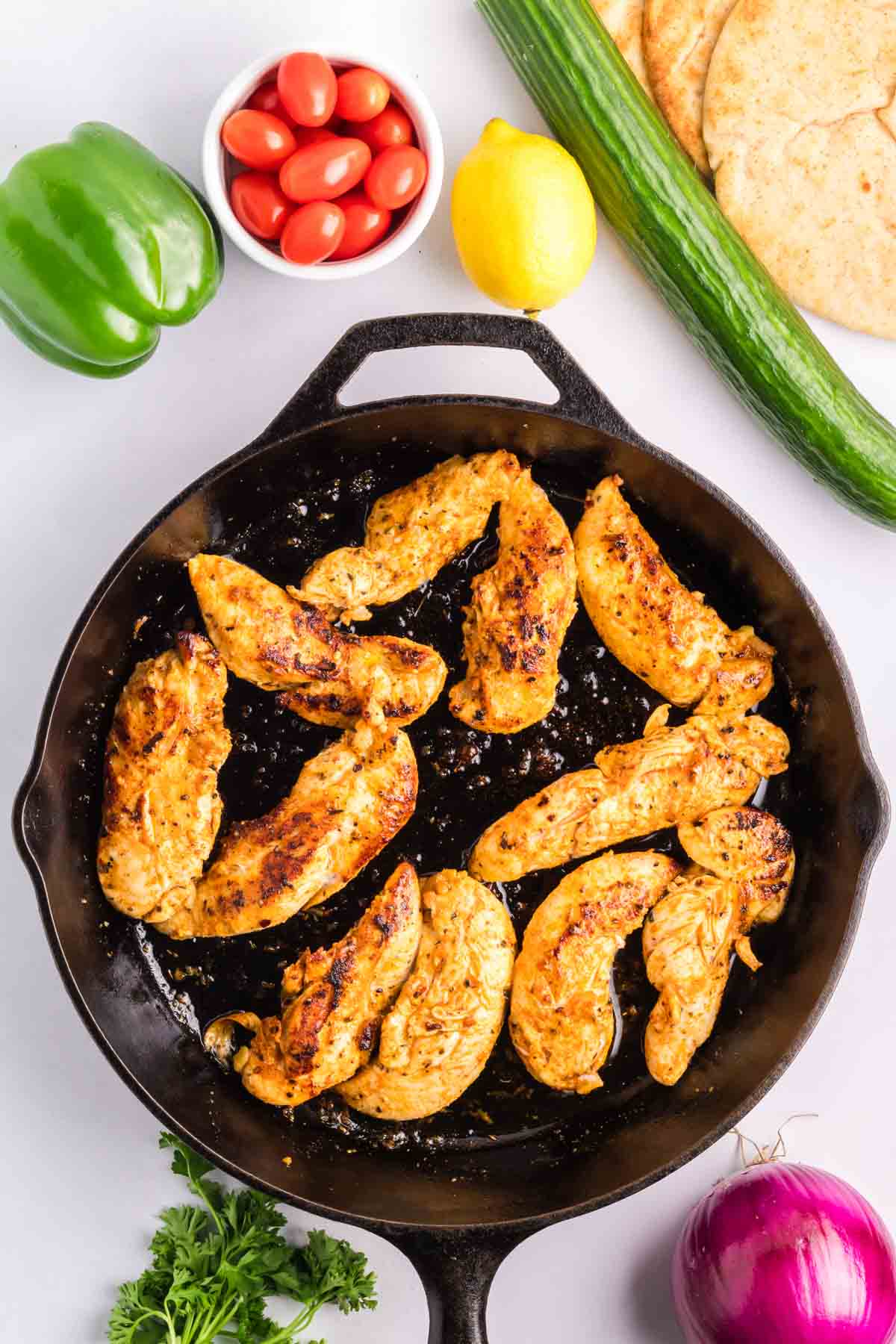 Chicken tenders in a skillet being cooked for greek chicken pitas.
