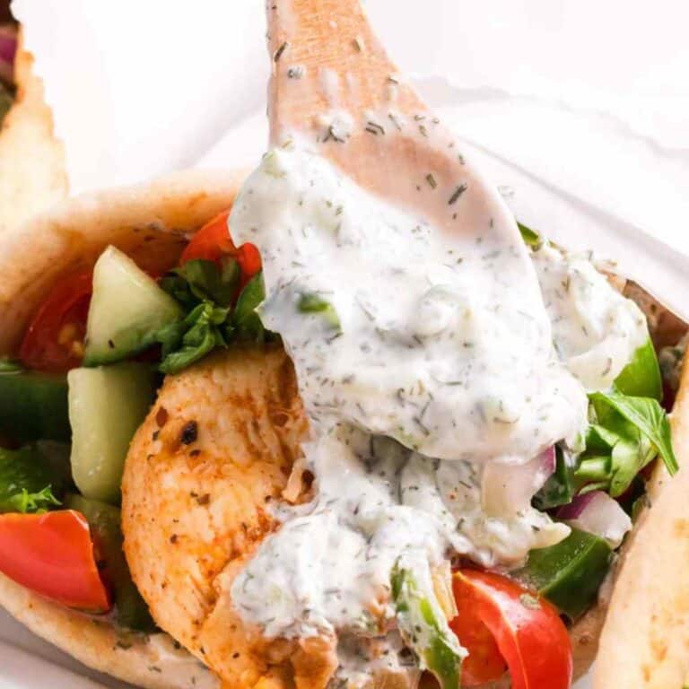Featured image show tzatziki sauce on a spoon being spooned over chicken pitas.
