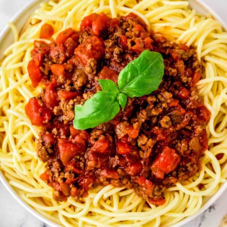 Pasta with meat sauce on a plate topped with basil.