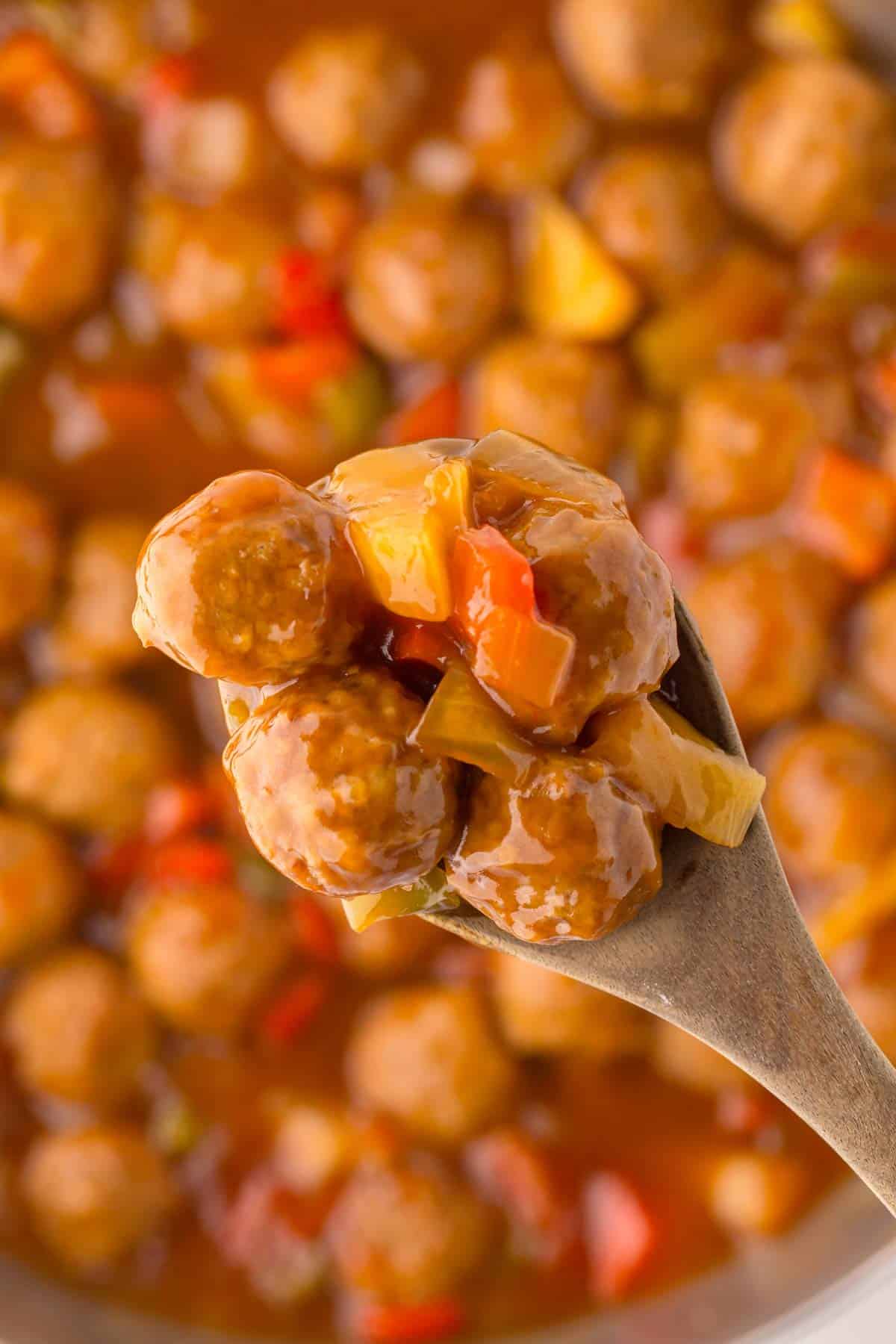 Close up of sweet and sour meatballs on a spoon.