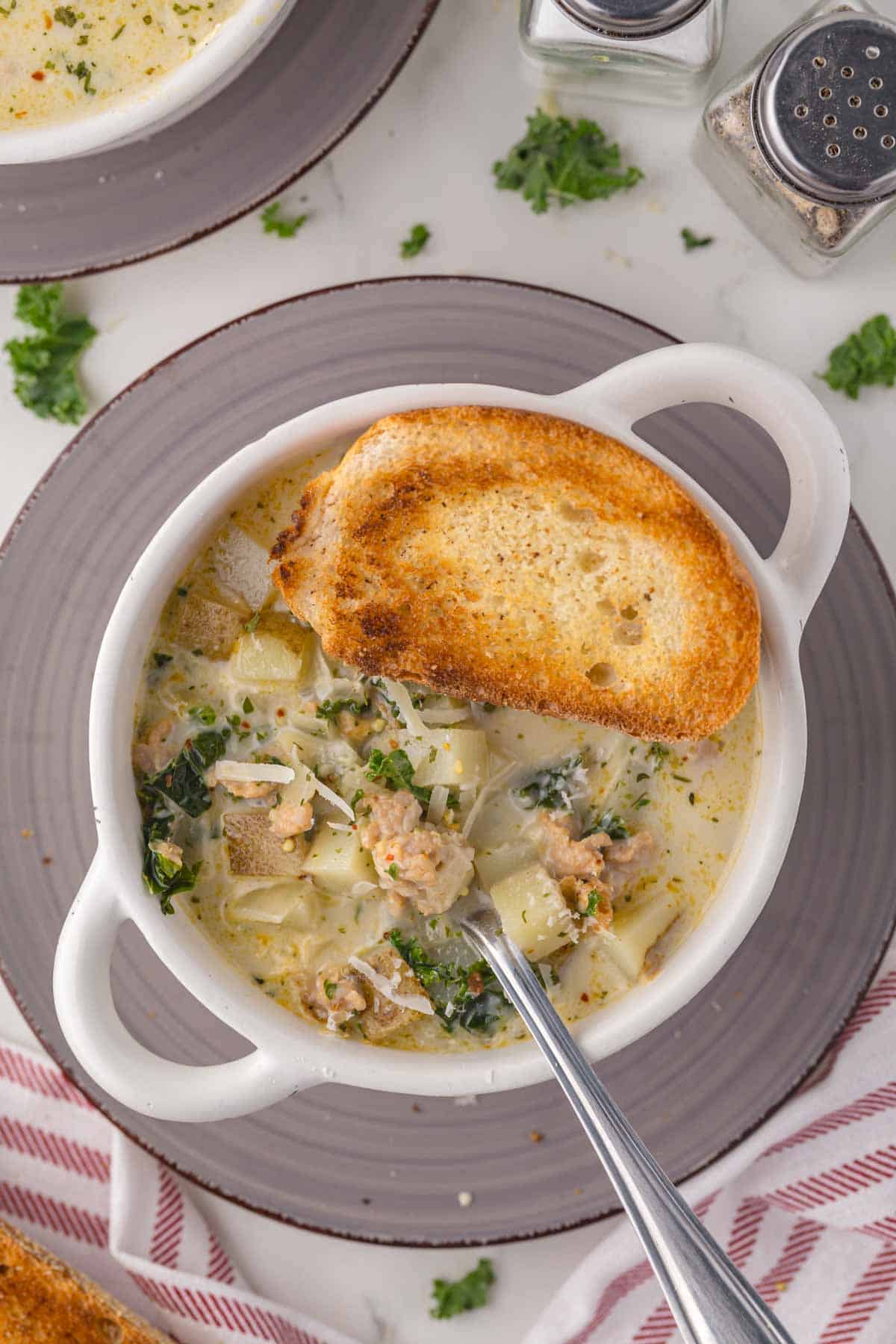A bowl of Trader Joe's Zuppa Toscana in a white bowl with a piece of bread.
