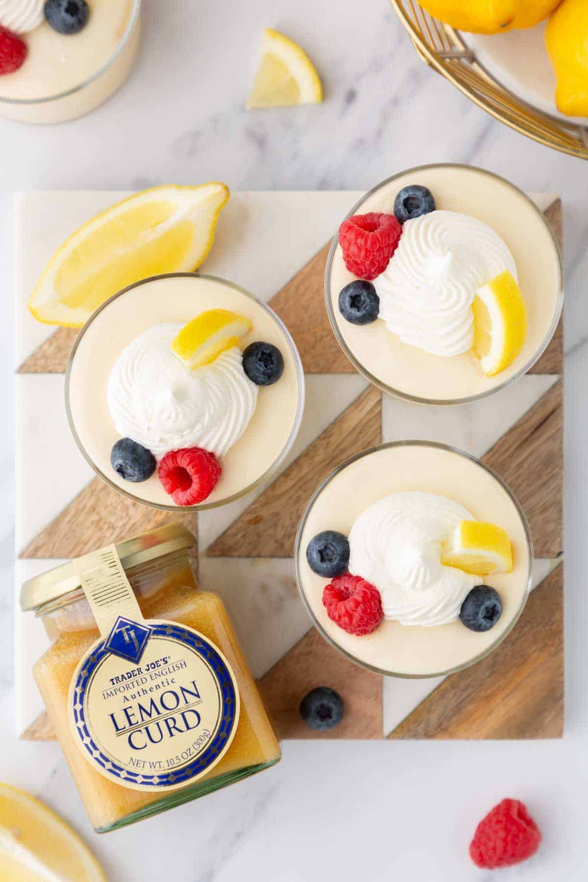 Three glass containers of lemon curd mousse topped with whipped cream and berries.