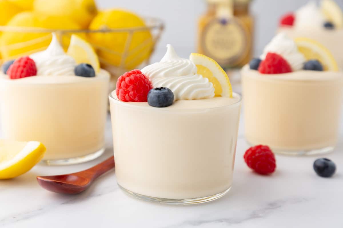 Three glass containers of lemon curd mousse topped with whipped cream and berries.