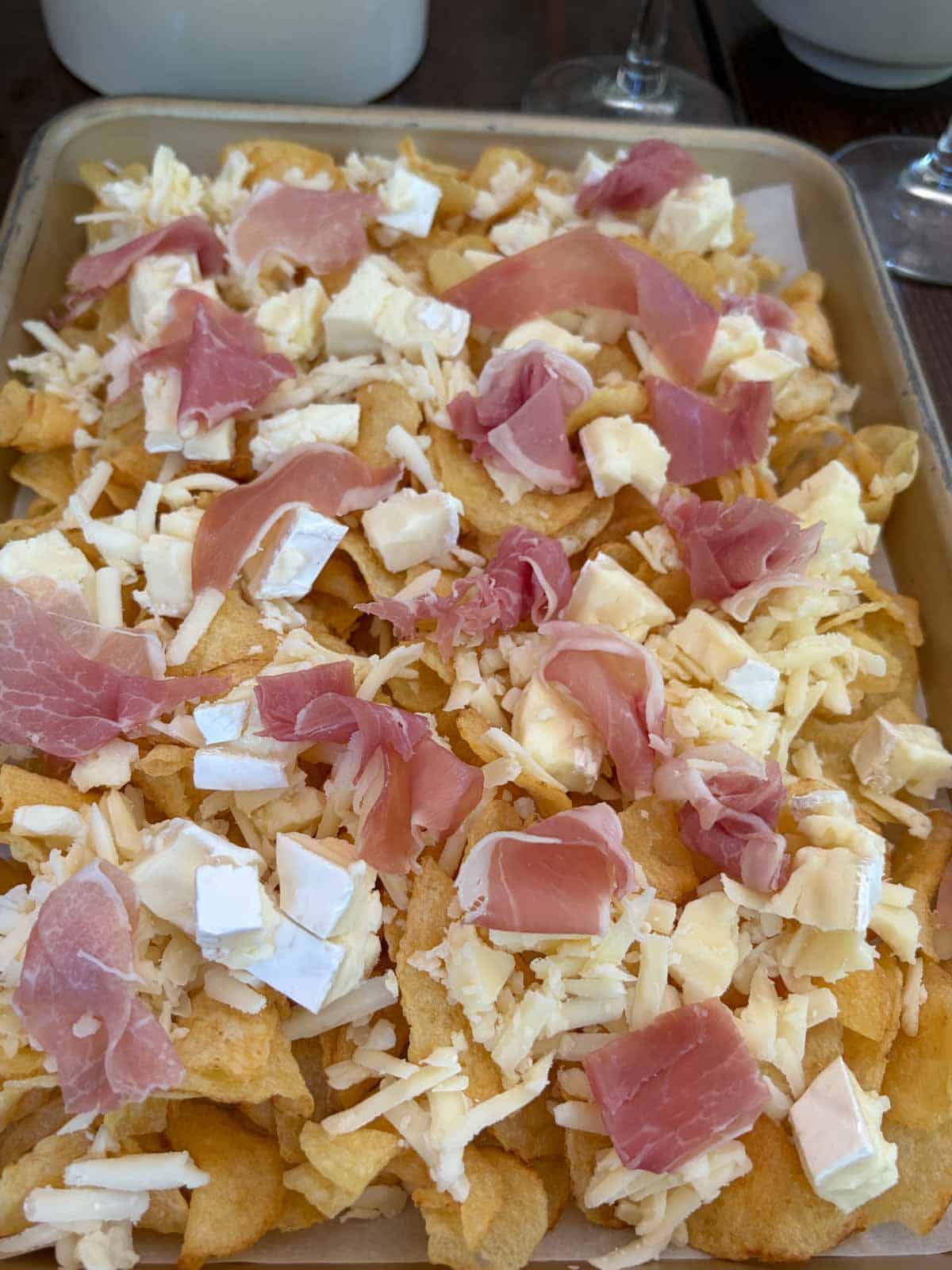 Kettle chips topped with cheese and meat on a baking sheet.