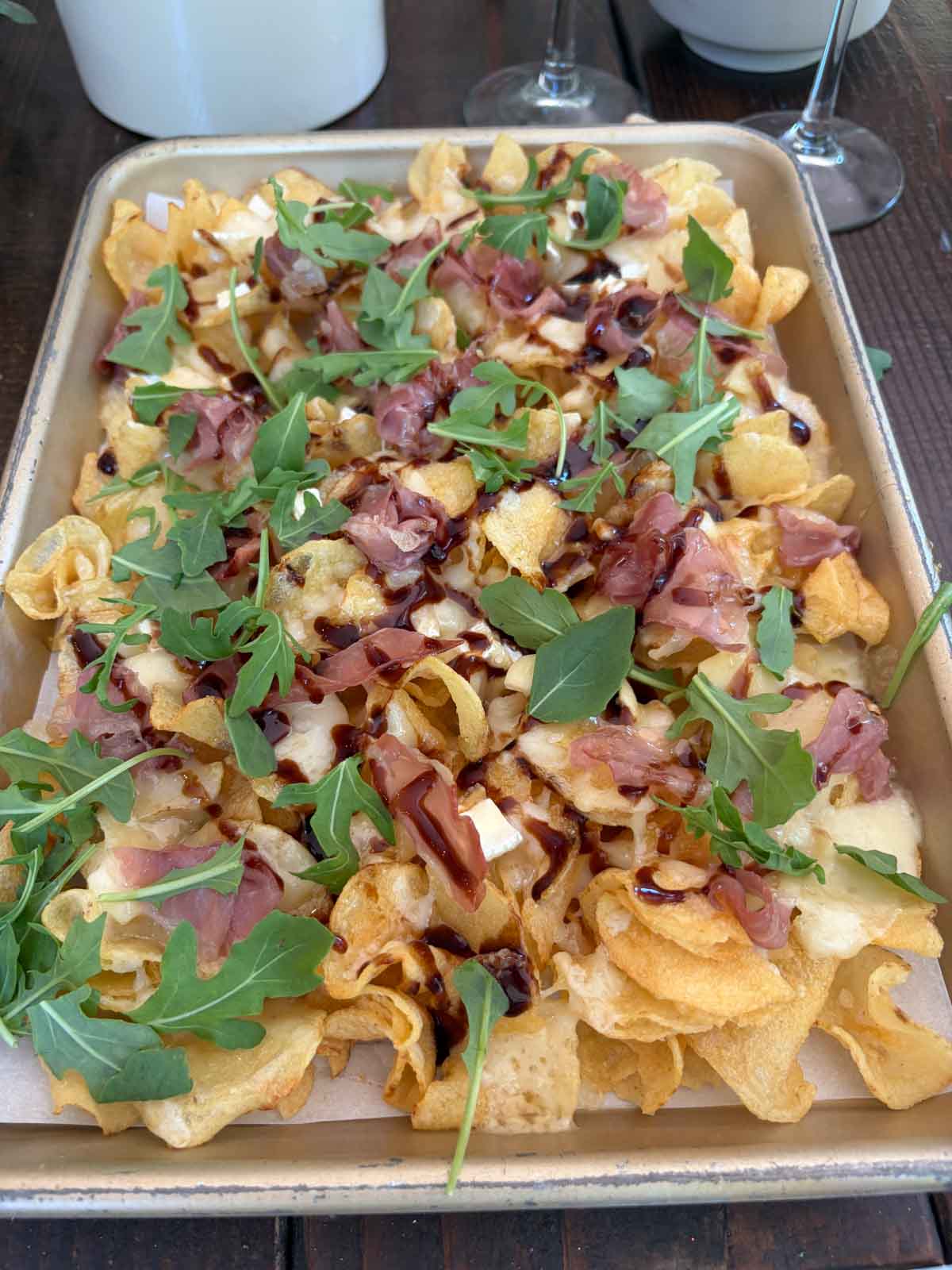 Charcuterie nachos on a baking sheet topped with arugula.